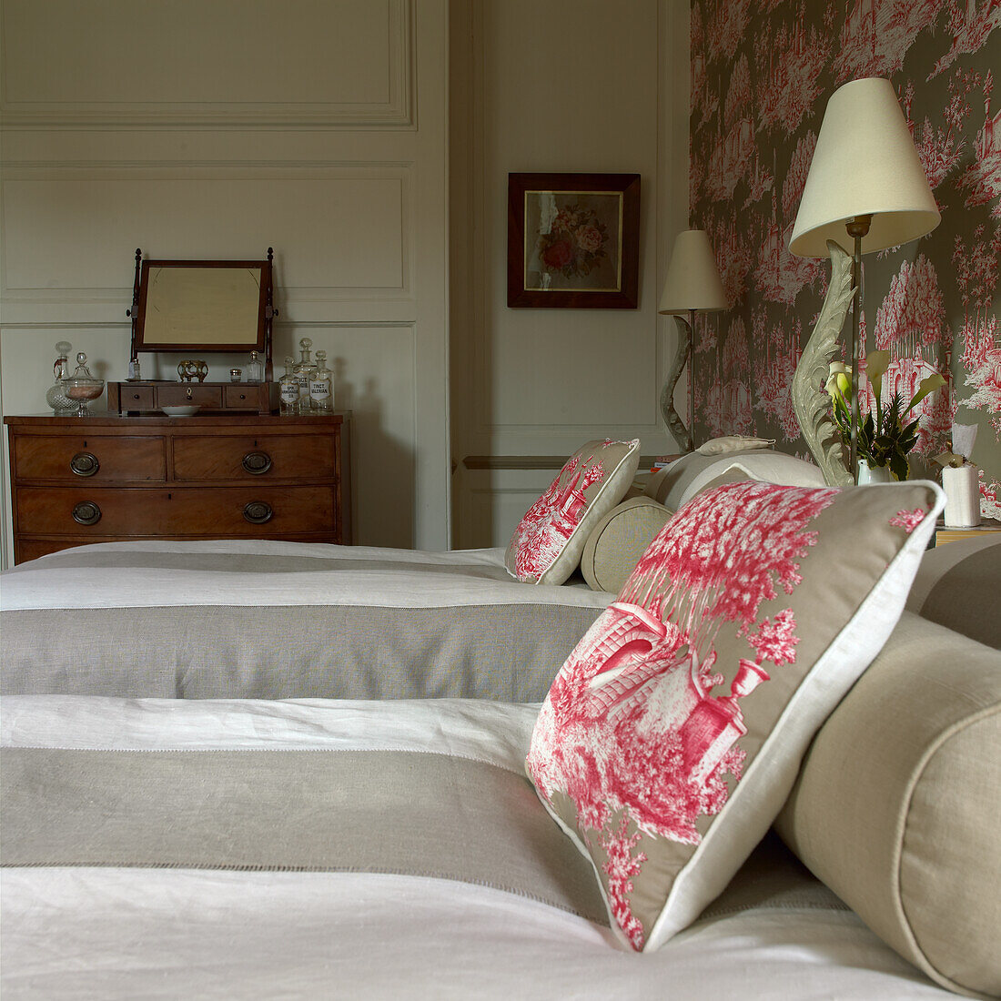 Bed with patterned cushions, wooden chest of drawers in the background