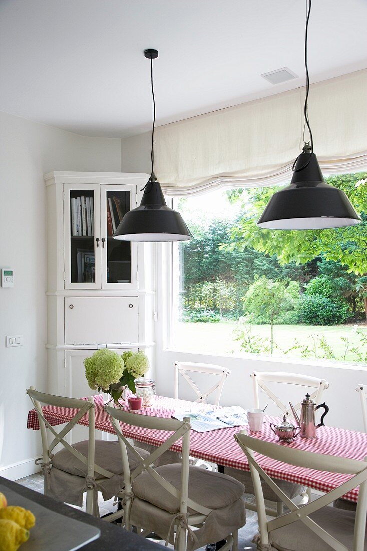 Country-house-style dining table and chairs in front of window and white corner cupboard in dining room