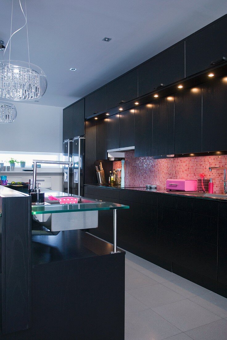 A black fitted kitchen with pink mosaic wall tiles and integrated spot lights
