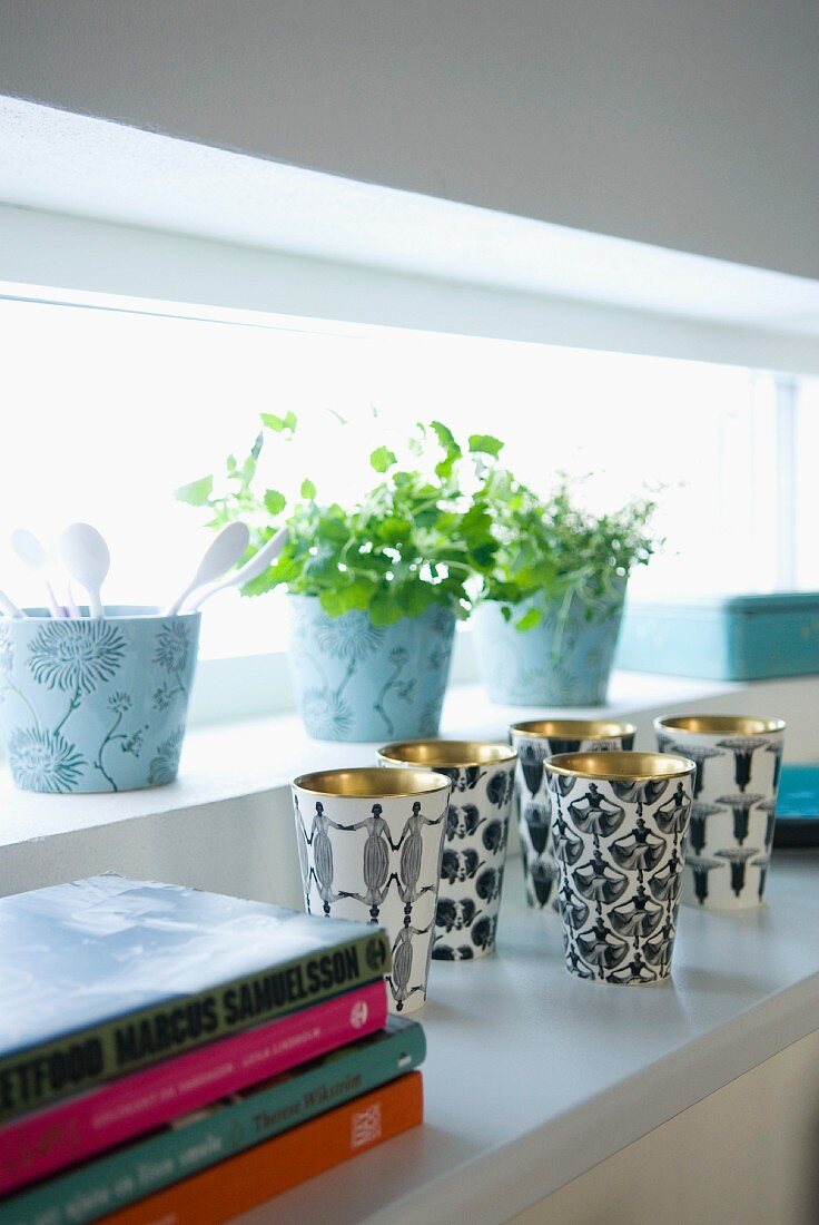 Golden cups with a black-and-white pattern and pots of herbs on the window sill of a long narrow window