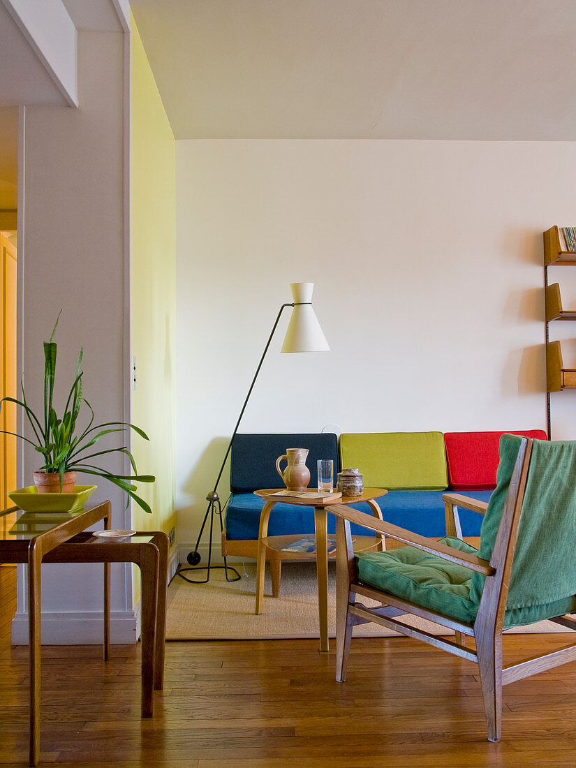 Wohnzimmereinrichtung aus den 50er Jahren mit farbiger Polsterung auf leichten Holzmöbeln, typischer Stehlampe und verschiedenen Beistelltischen