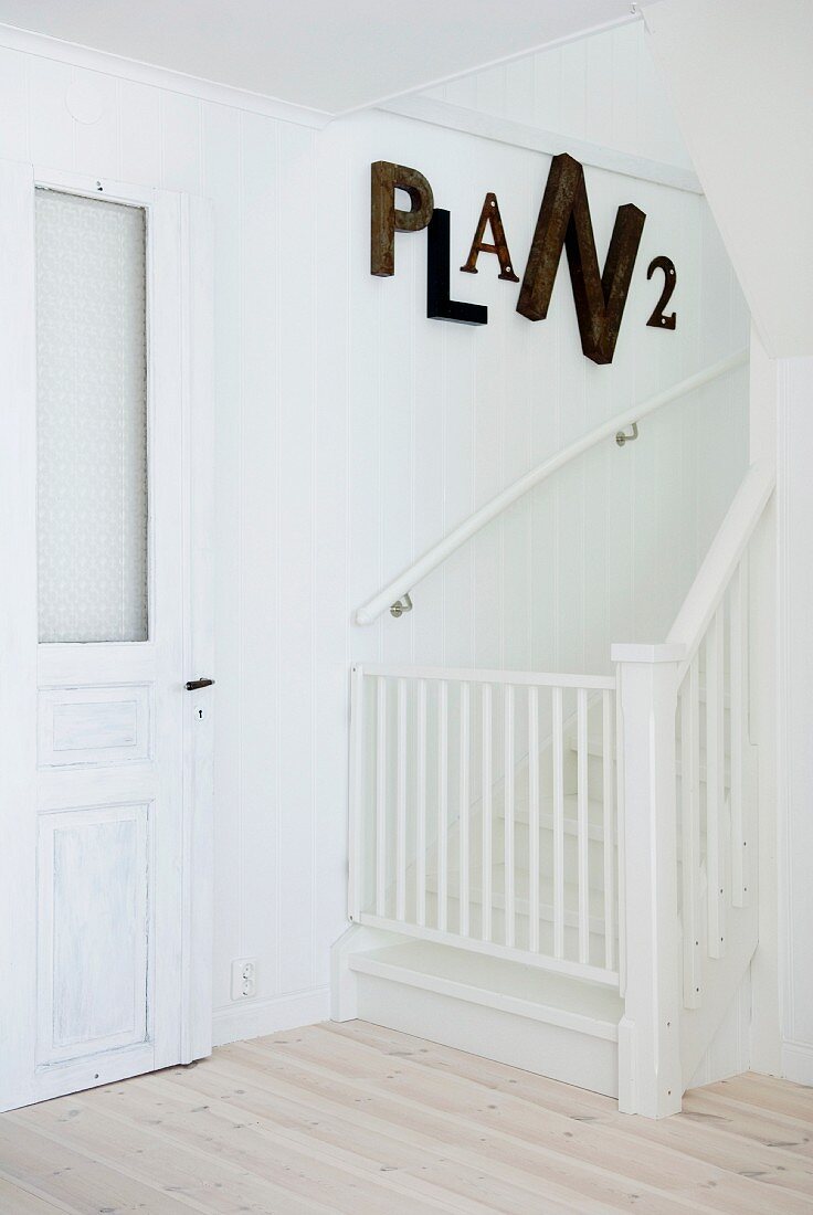 Treppenaufgang in Weiß mit Schutzgitter und grossen Buchstaben an der Wand