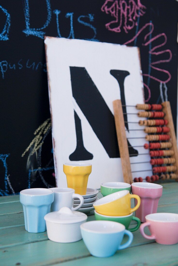 Colourful cups, vintage abacus and board with large letter on surface in front of blackboard