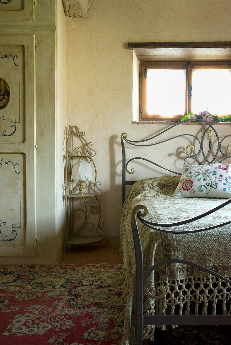 Metal bed with patterned cushions in bedroom with oriental carpet