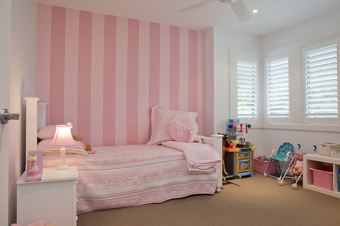 Romantisches Mädchenzimmer in Rosa und Weiß - Vintage Bett vor gestreifter Tapete in Rosa an Wand