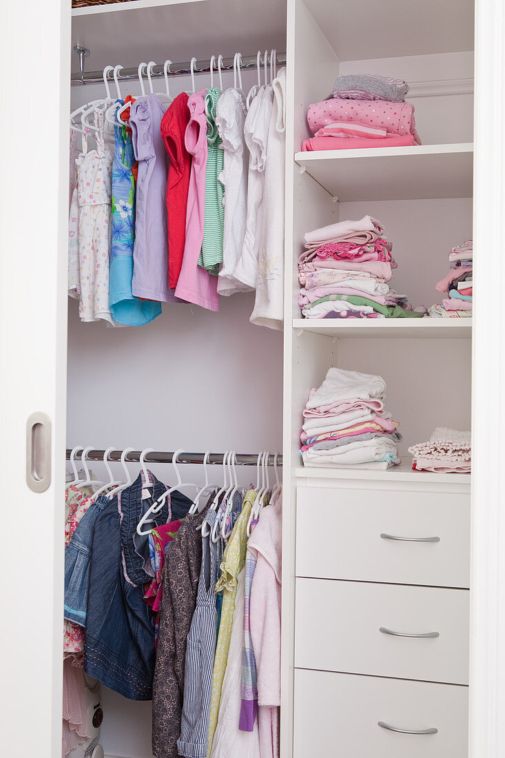 Children's clothing hanging in open-fronted wardrobe with drawers in shelving compartments