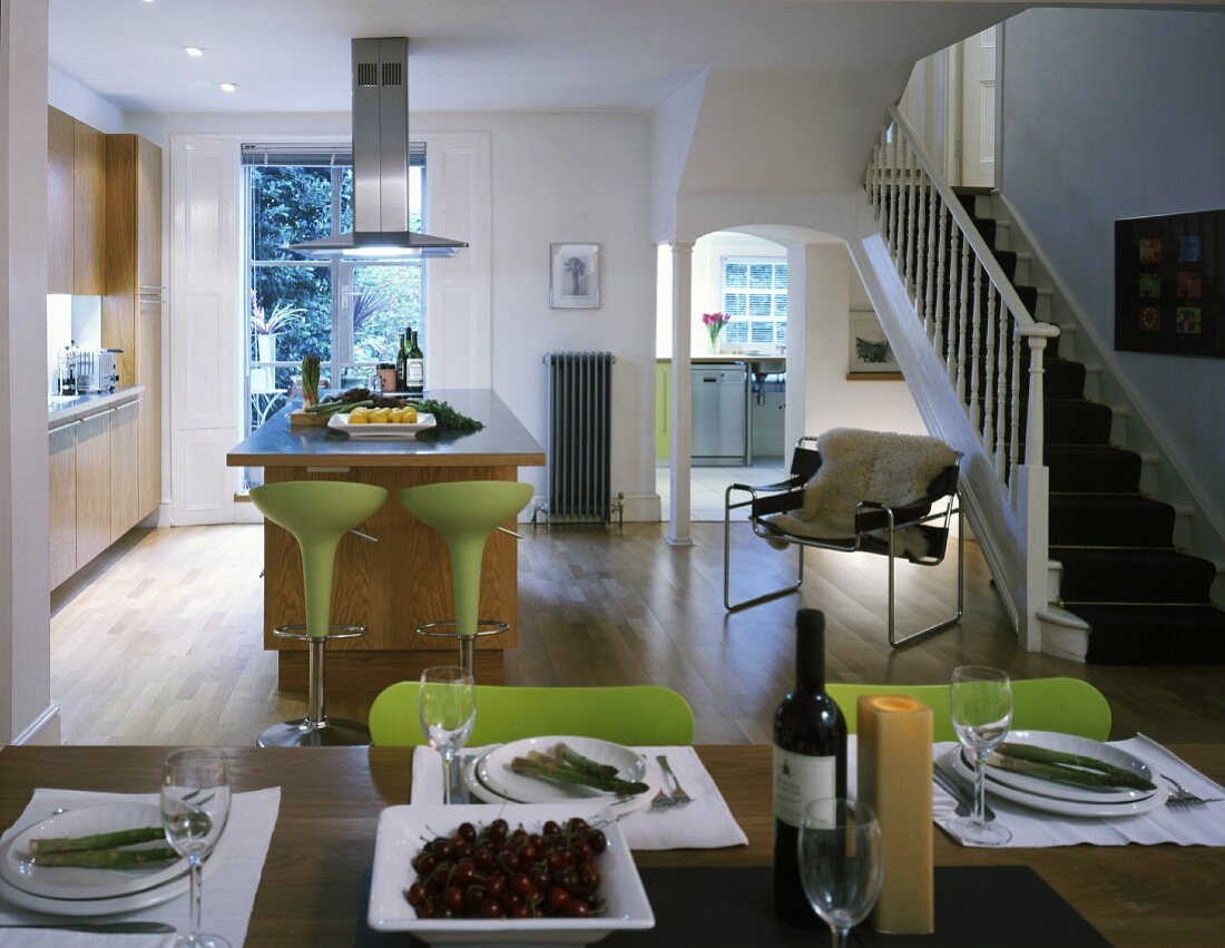 Gedeckter Tisch und Barhocker an freistehendem Küchenblock im offenen modernisierten Wohnraum