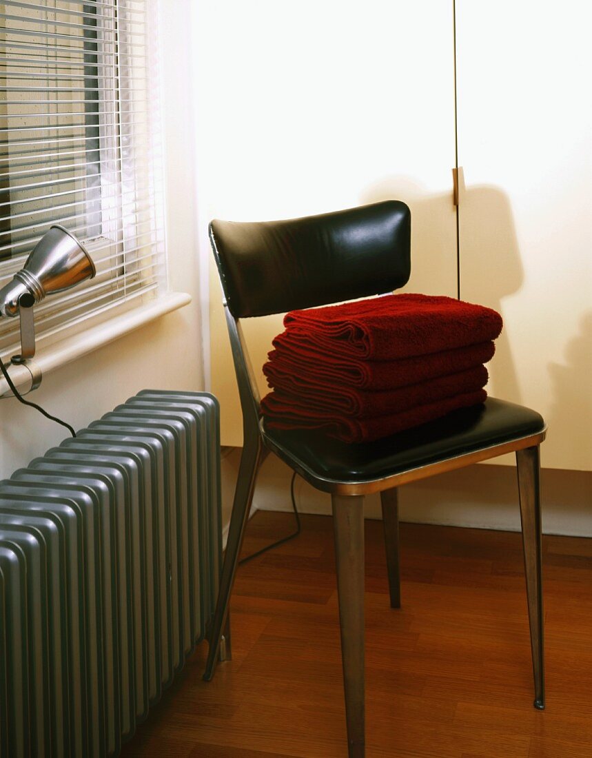Metallstuhl mit schwarzem Lederbezug auf Sitz- und Rückenpolster neben silbergrau lackiertem Heizkörper