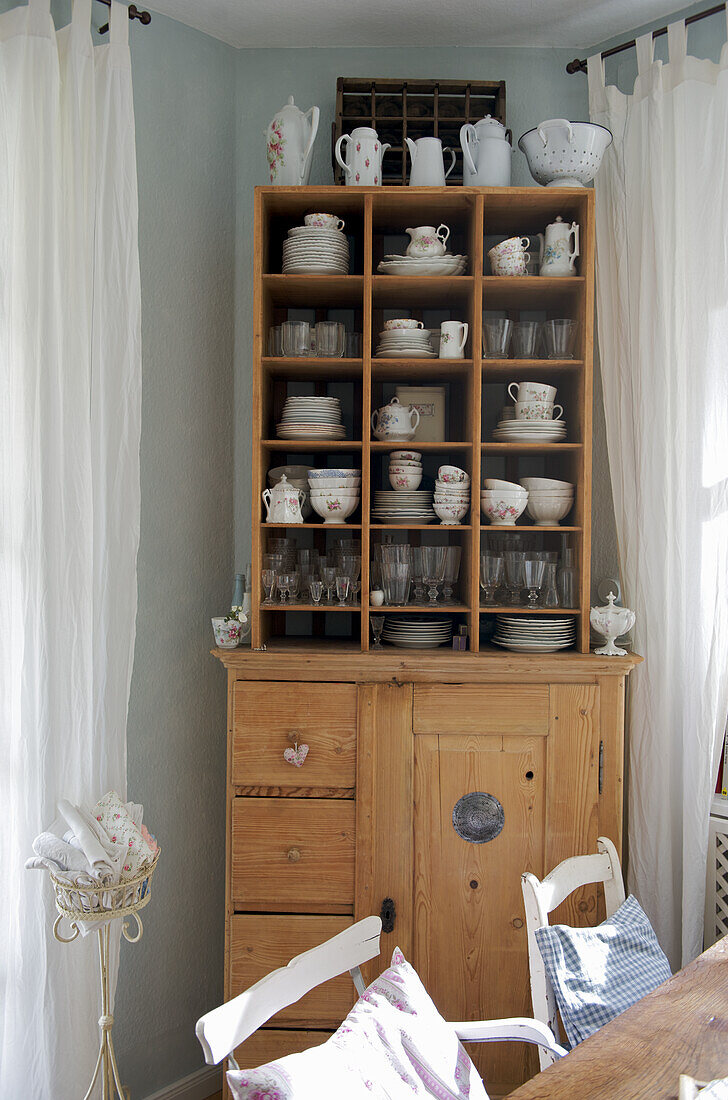 Wooden display cabinet with country-style crockery and white curtains