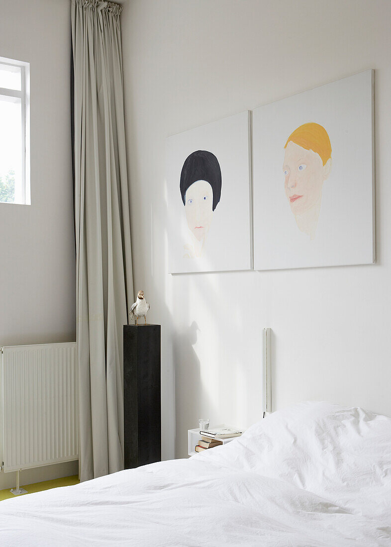 Minimalistisches Schlafzimmer mit Porträtgemälden über dem Bett