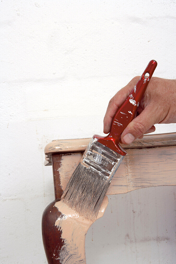 Hand holding a flat brush painting an antique table with curved legs