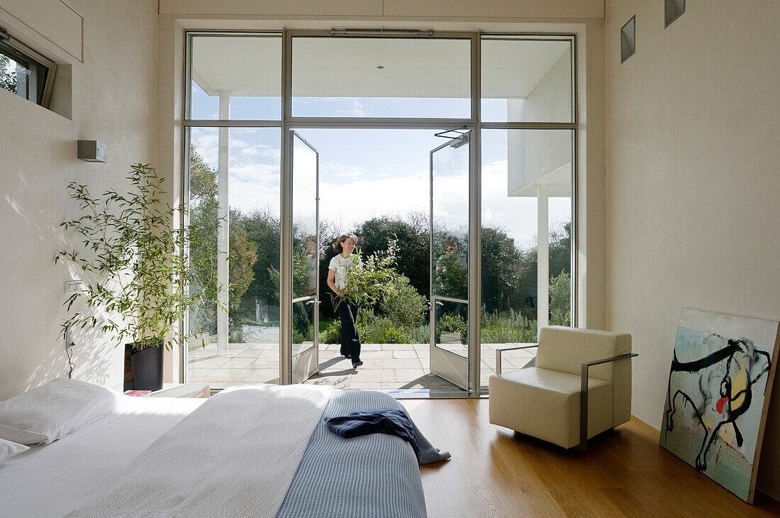 Helles Schlafzimmer mit Terrassentüren und Person mit Blumenstrauß