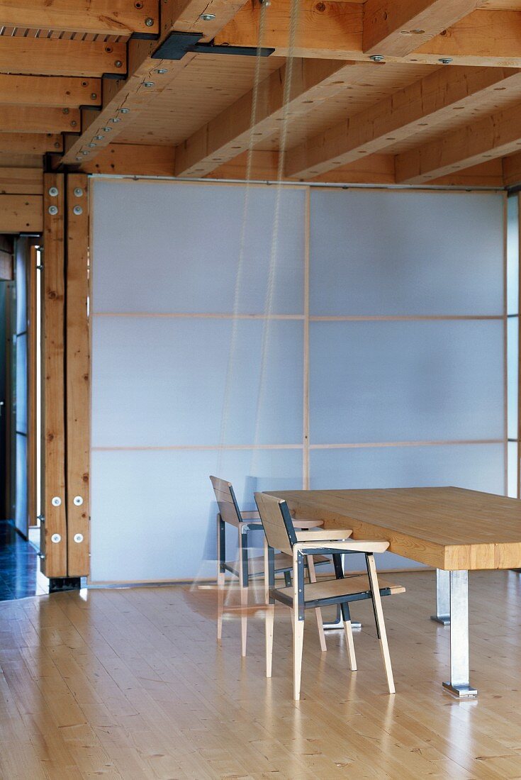 Essplatz mit massiver Tischplatte vor transluzenter Trennwand in modernem Holzhaus