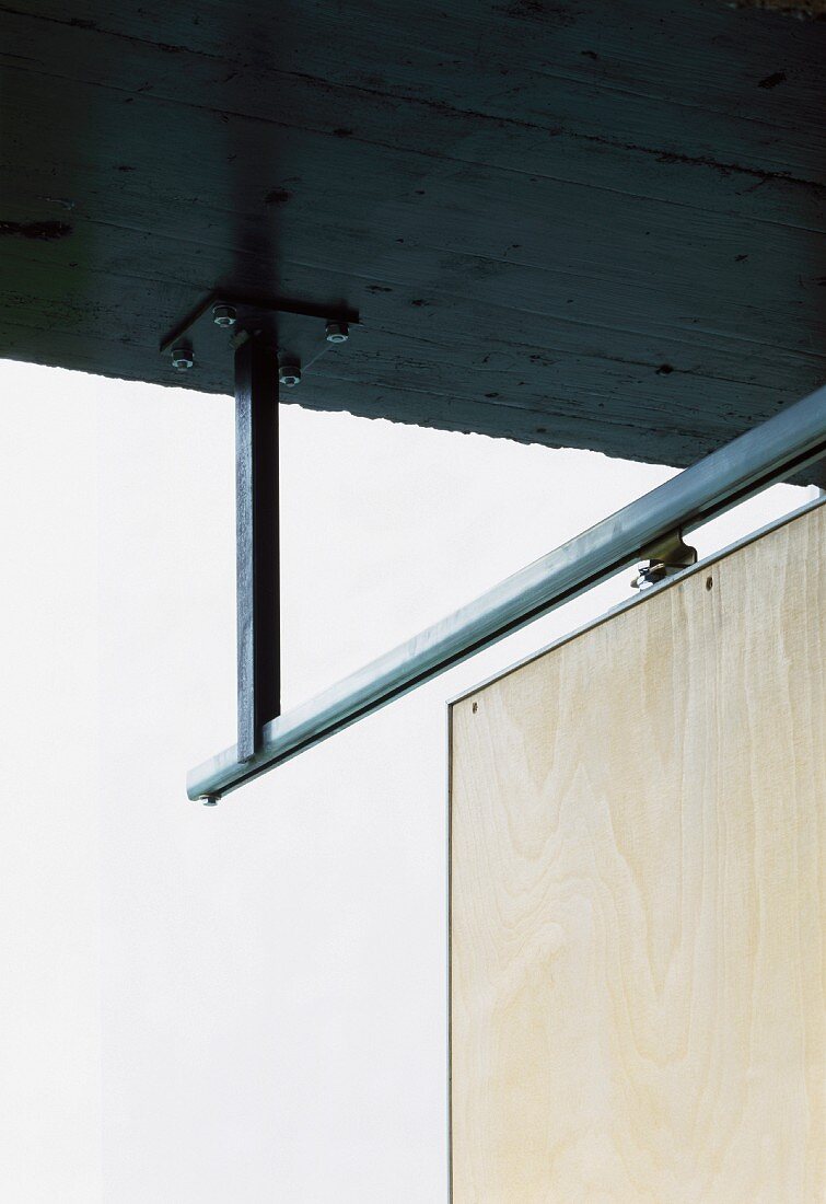 Stahlgerahmte Holztür an von Betondecke abgehängter Schiebeschiene im Gegenlicht