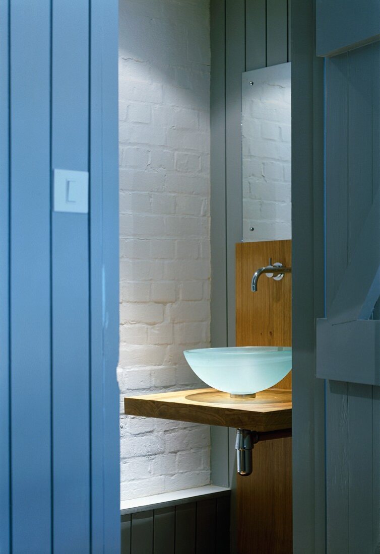 Wood-clad walls, white brick wall and view of glass basin on wooden washstand through open plank door