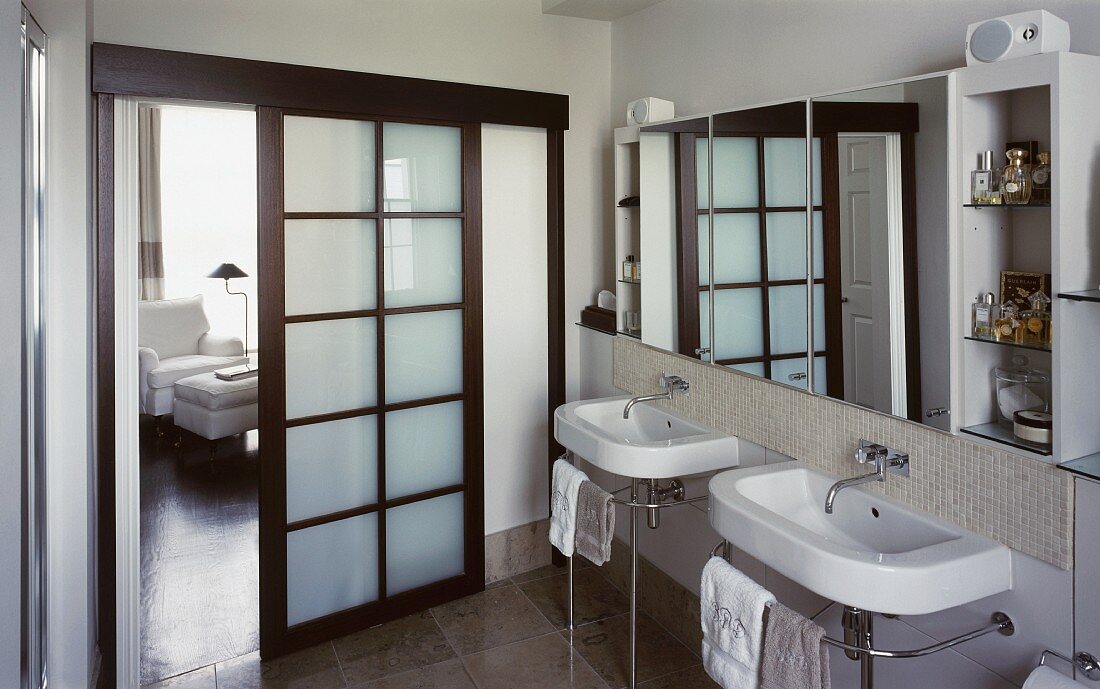 Bathroom with washstands on metal frames and open sliding wooden door with panels of opaque glass