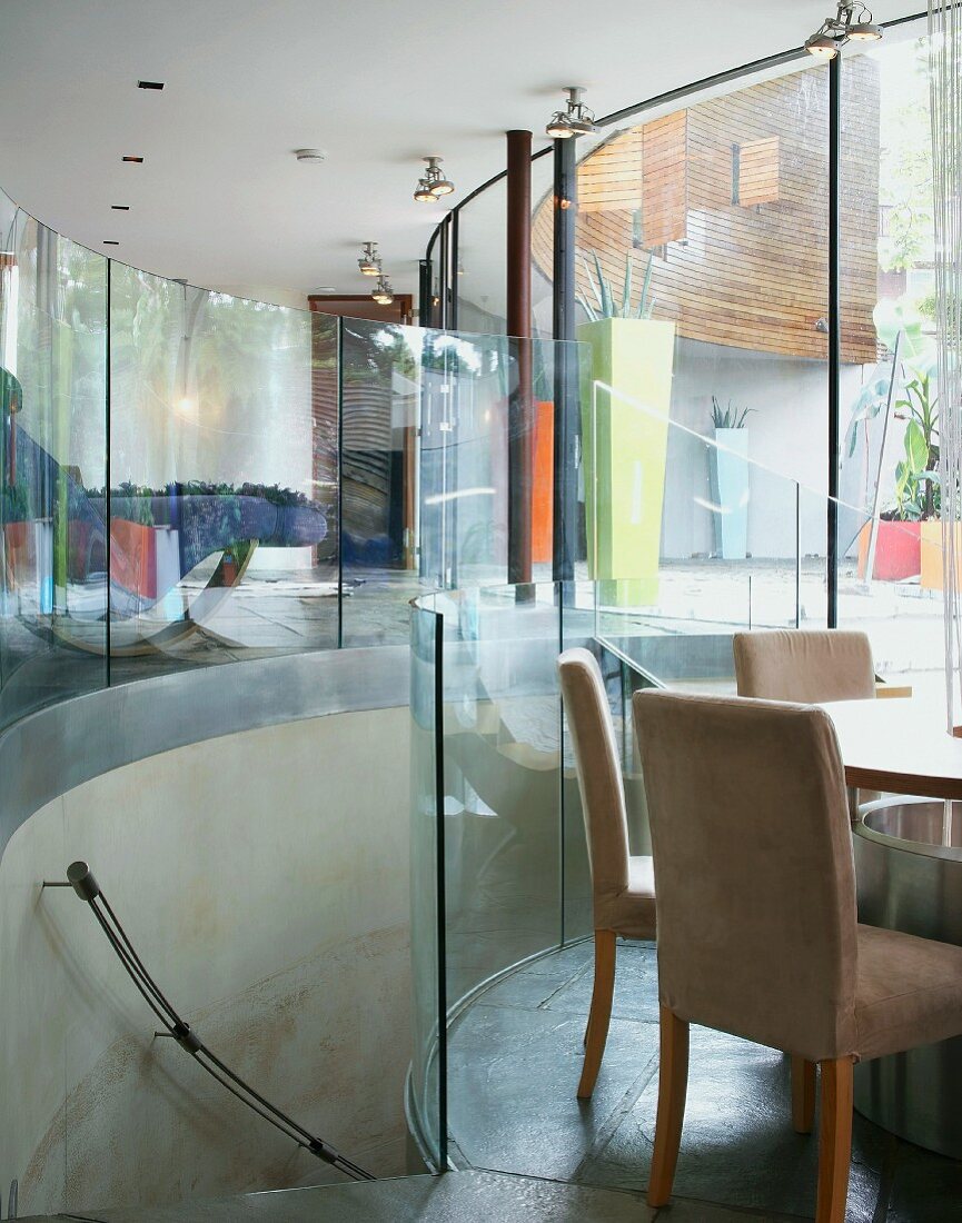 Zeitgenössische Architektur mit halbrundem Treppenabgang und Glaswänden zwischen Wohnraum und tieferliegendem Essplatz