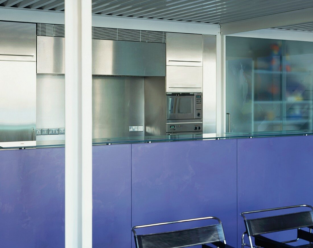 Lavendelfarbene Küchentheke und schwarze Bauhaus-Sessel vor Edelstahlküchenzeile