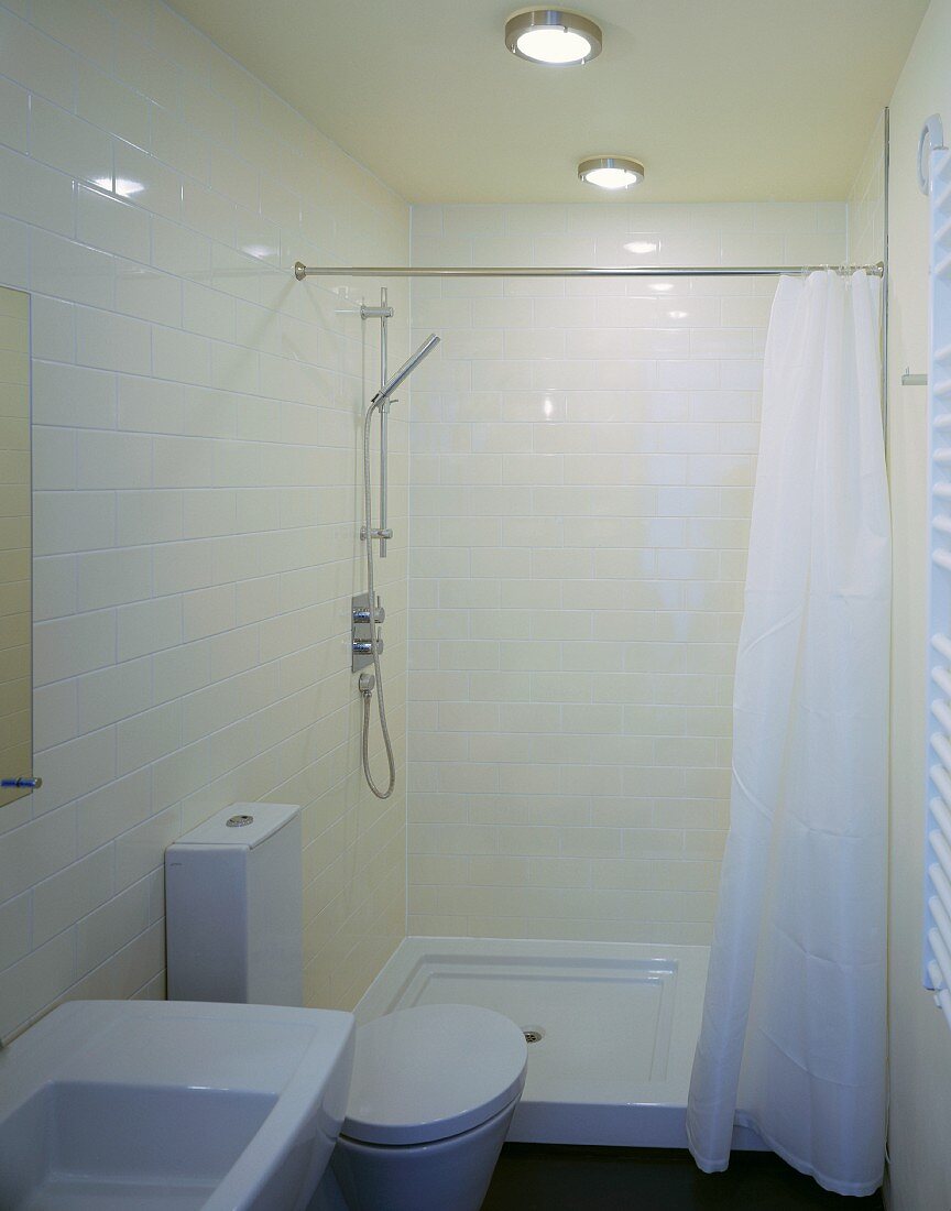 Kompakt auf engem Raum - cremefarbene Fliesen und weiße, moderne Badeinrichtung mit maritimen Deckenlampen