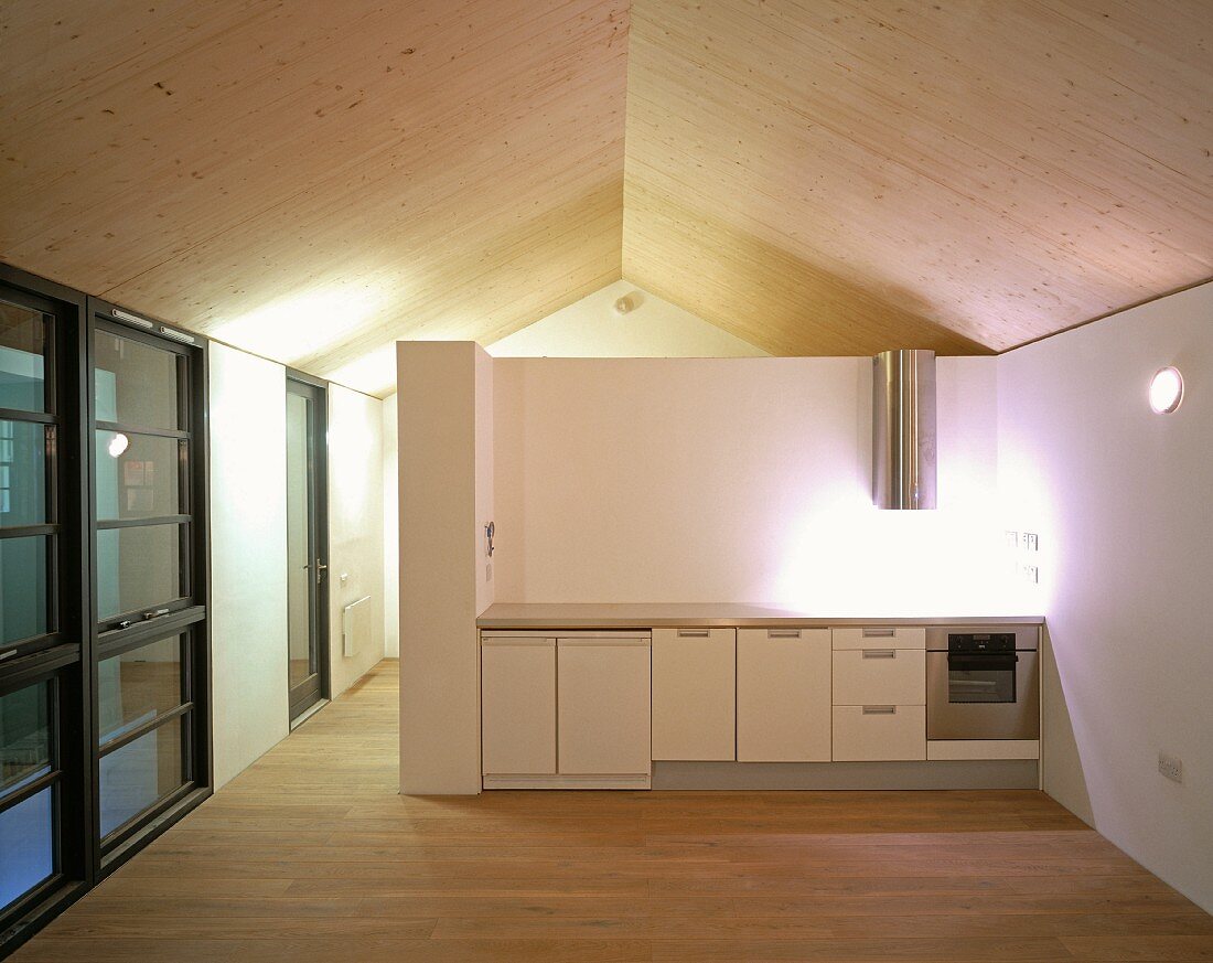 Offener Dachraum mit einfacher Küchenzeile unter Spotlicht an halbhoher Trennwand
