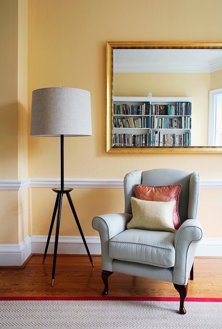 Retro standard lamp and classic armchair below gilt-framed mirror in traditional room