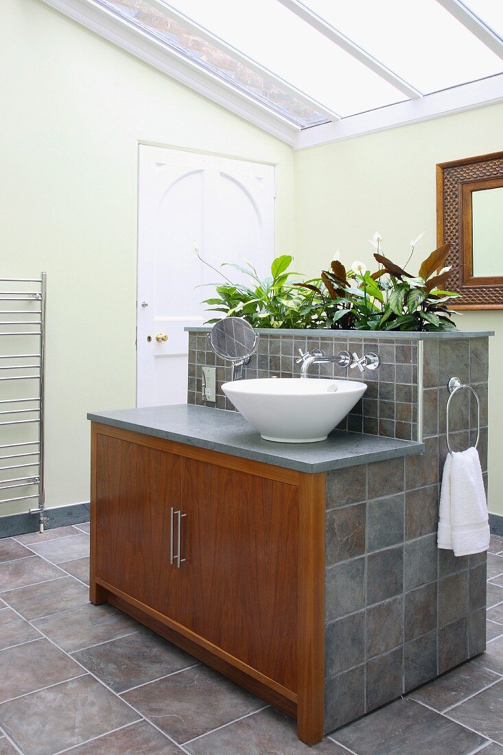 Modernes Bad mit Glasdach und grauen Fliesen, Holztüren an zentralem Waschtischblock mit integriertem Pflanzentrog