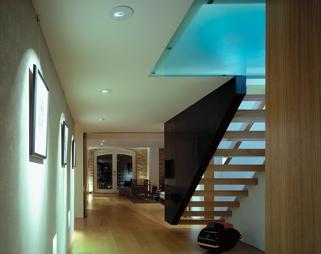 Floating staircase between wall and dark stringer element with indirect light through glass ceiling
