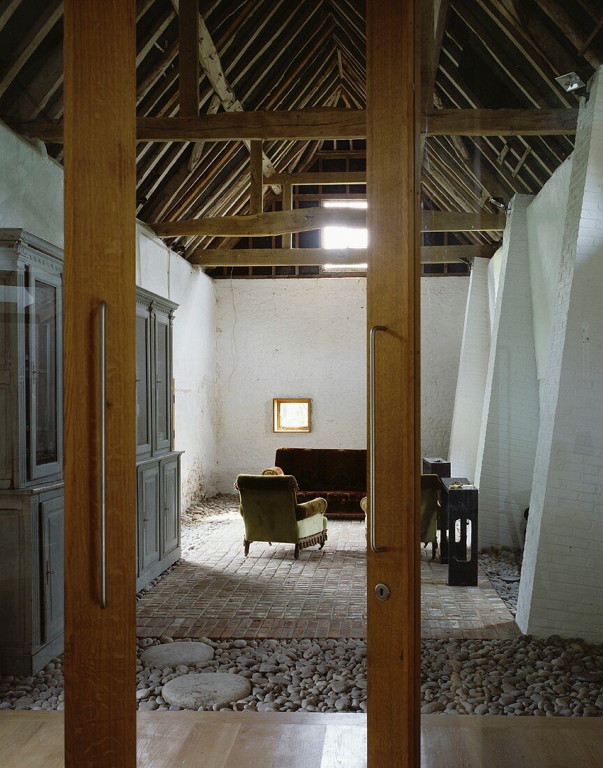 Blick durch halb geöffnete Glastür auf historischen Dachraum mit antiken Polstermöbeln und Anrichte, am Boden Kiesel und Terracottafliesen
