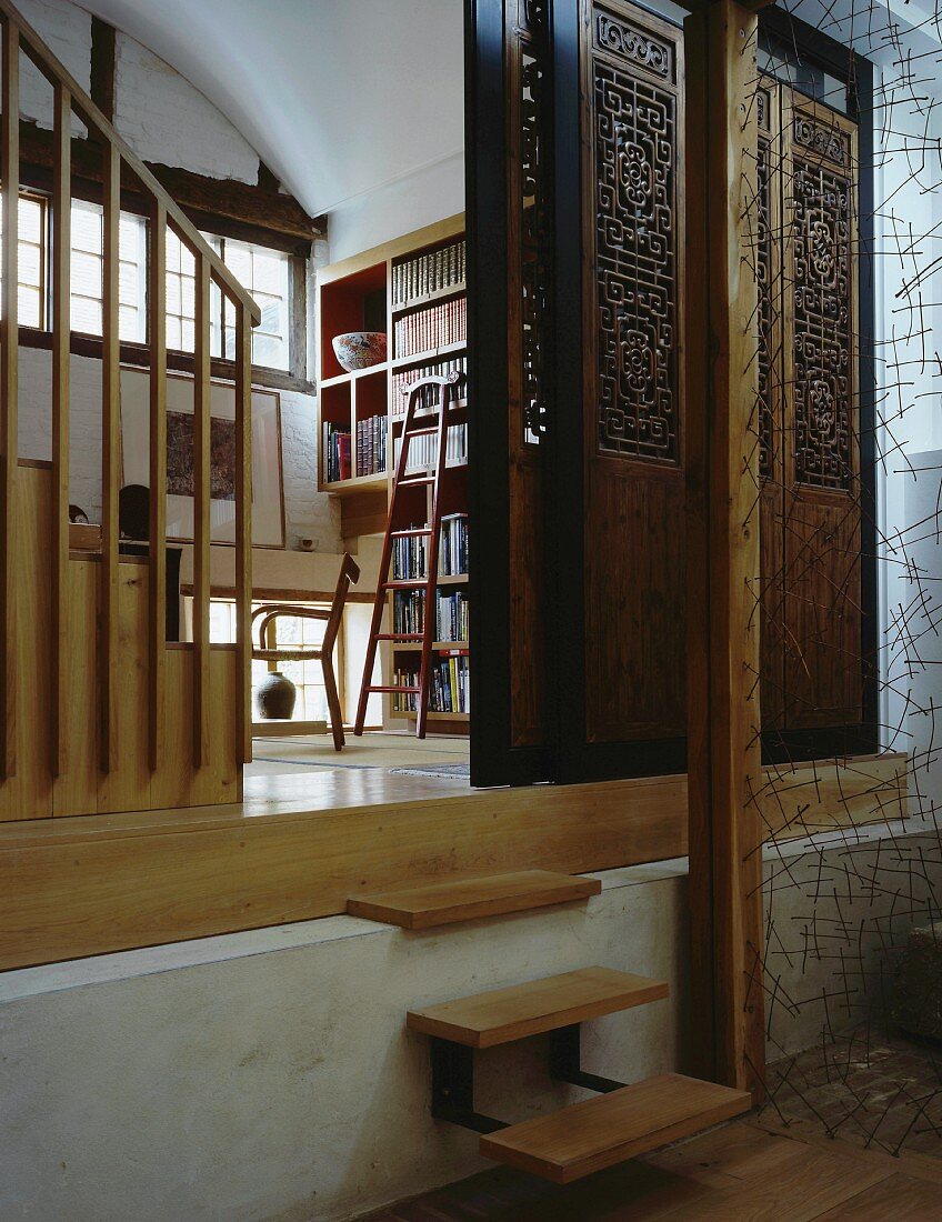 Sliding wall made from antique, carved wooden elements in front of library and delicate, sculptural wire partition