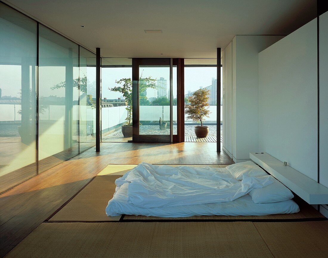 Modernes Schlafzimmer im japanischen Stil mit Futon auf Tatami-Matten und Blick auf japanischen Terrassengarten vor Stadtkulisse