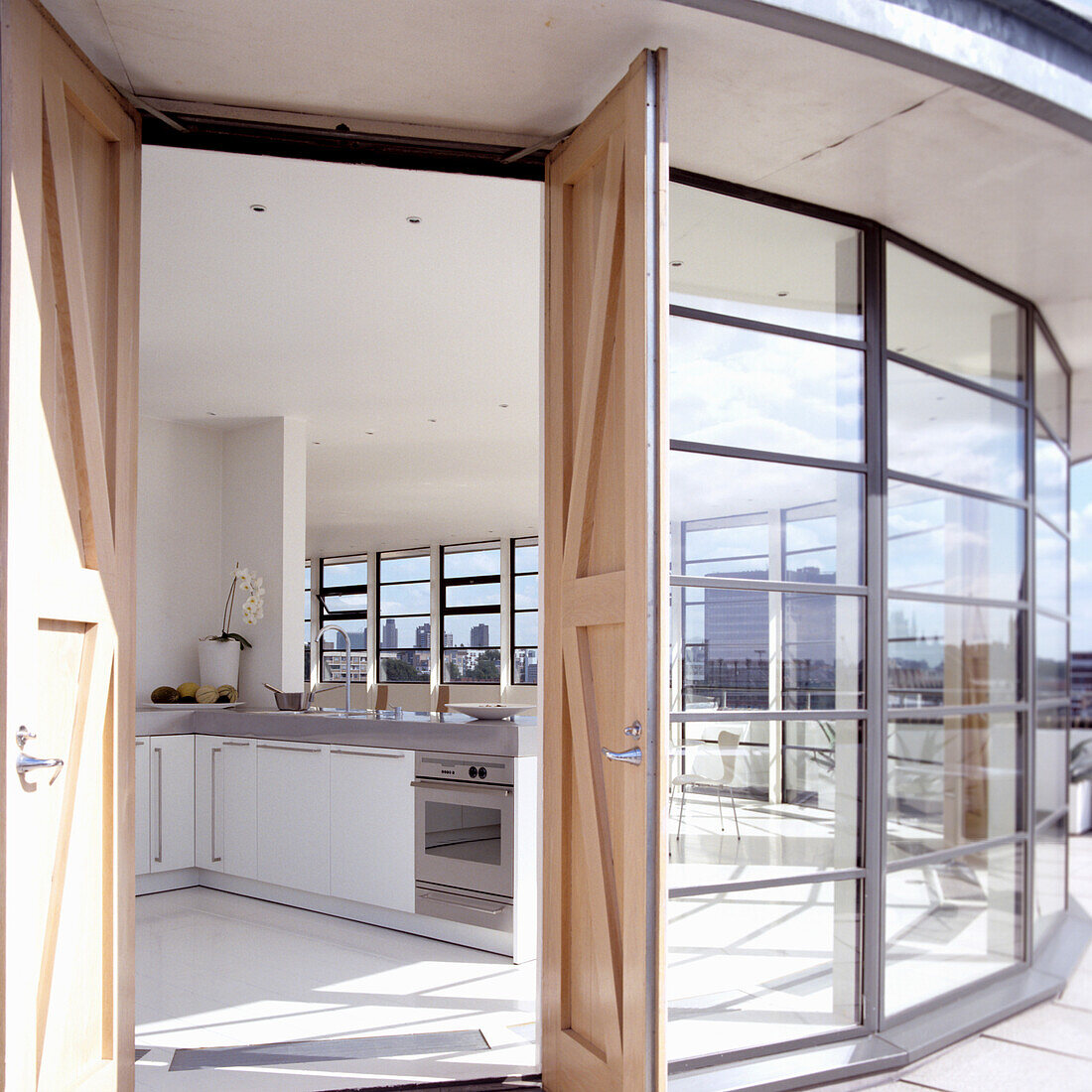 Open-plan kitchen with white furniture and a view of the city through floor-to-ceiling windows