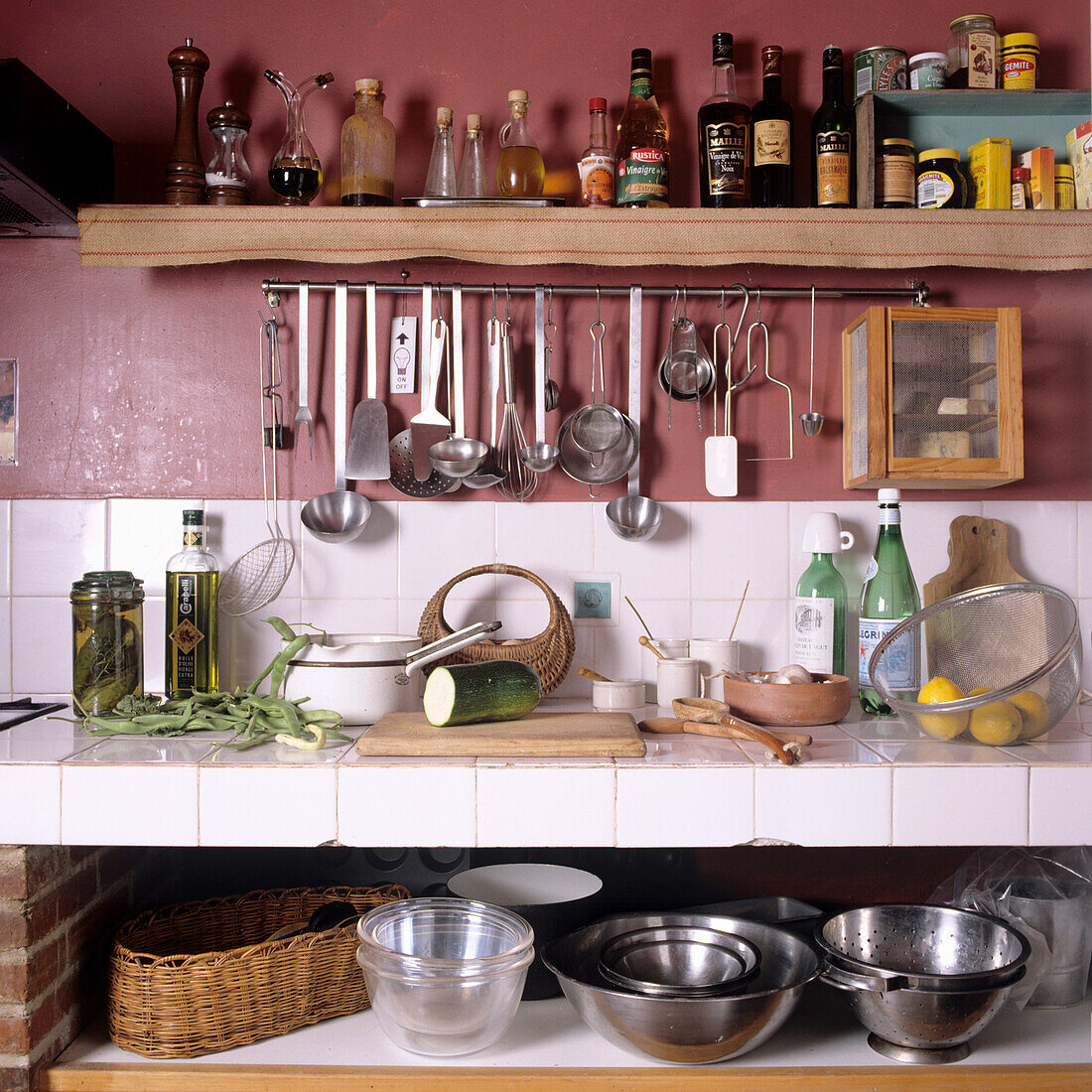 Shelf with spices and cooking utensils above white tiled kitchen worktop