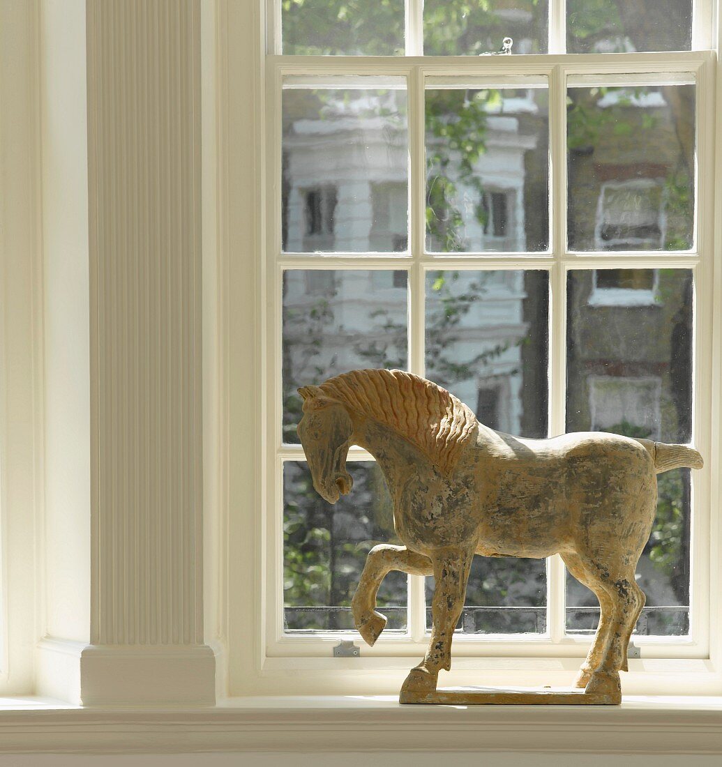 Pferde-Skulptur auf Fensterbrett vor Sprossenfenster