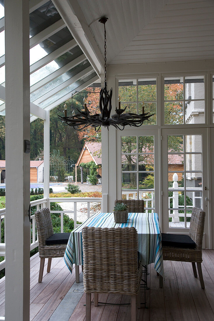 Wicker chairs at table with striped tablecloth on terrace of country house