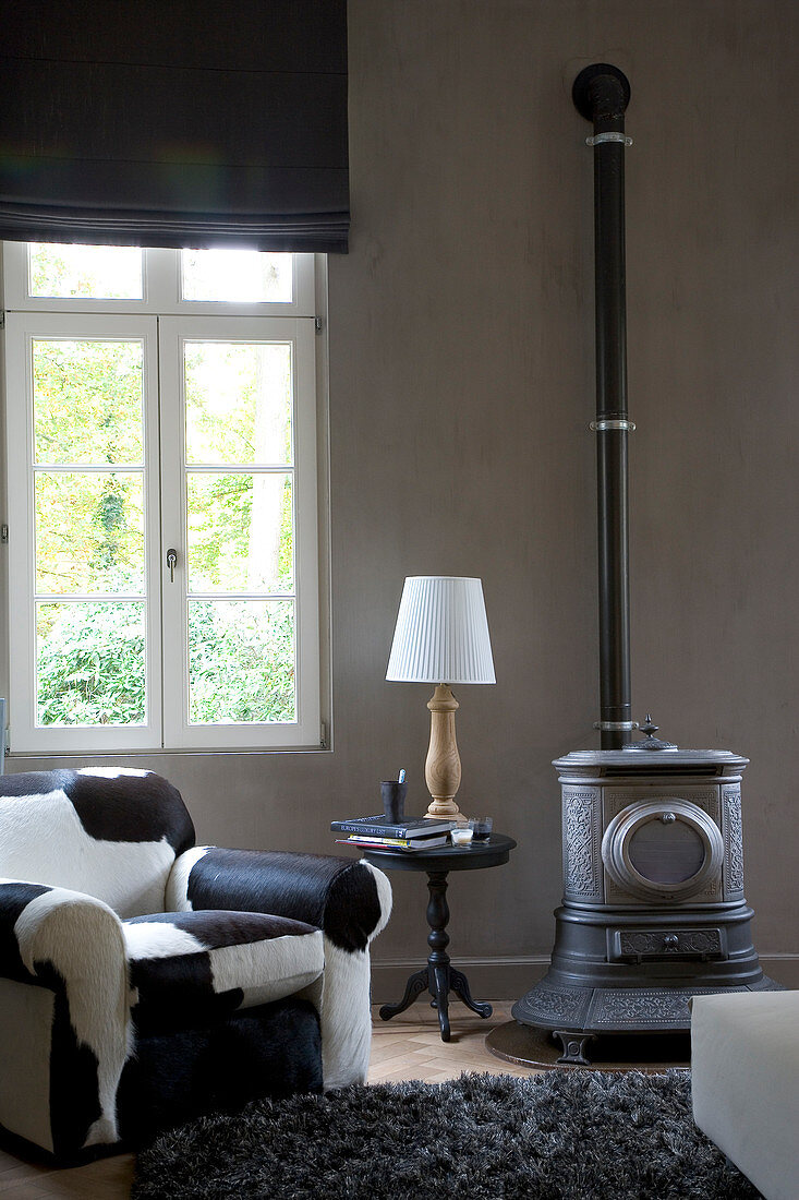 Sessel mit Fellbezug neben Beistelltisch und Kanonenofen im Retrostil in modernem Wohnzimmer