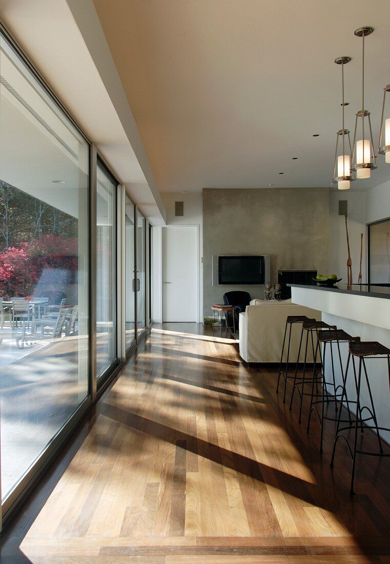 Living space with bar, stools and long glass wall leading to terrace