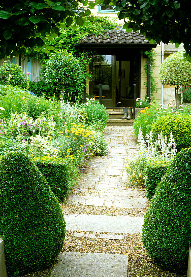 Gepflasterter Gartenweg mit abgestuften Staudenbeeten und Buchsbaumhecken