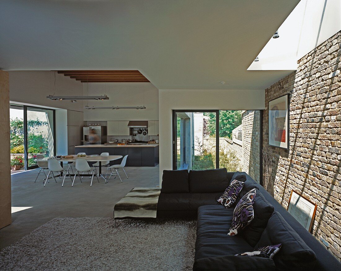 Blick vom Wohnzimmer mit schwarzem Sofa in den Ess- und Küchenbereich in zeitgenössischem Wohnhaus