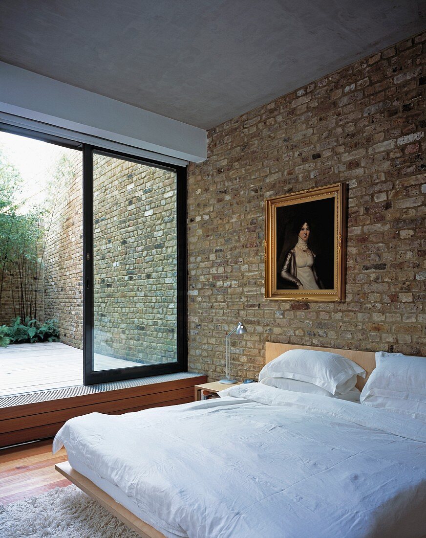 Modernes Schlafzimmer mit Ziegelwand, antikem Gemälde mit Goldrahmen und Blick in den Innenhof