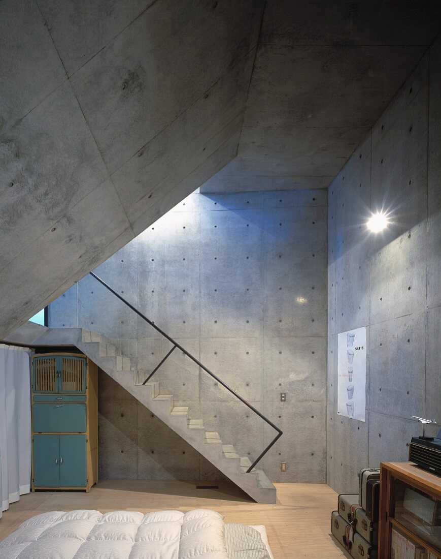A bedroom with concrete wall and a slanted ceiling and a flight of concrete steps