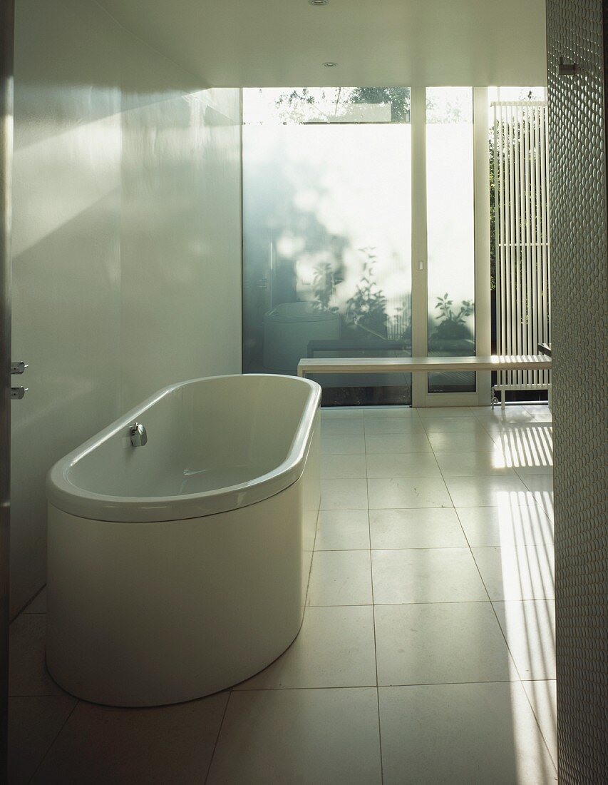 Minimalist bathroom with free-standing, white bathtub on tiled floor