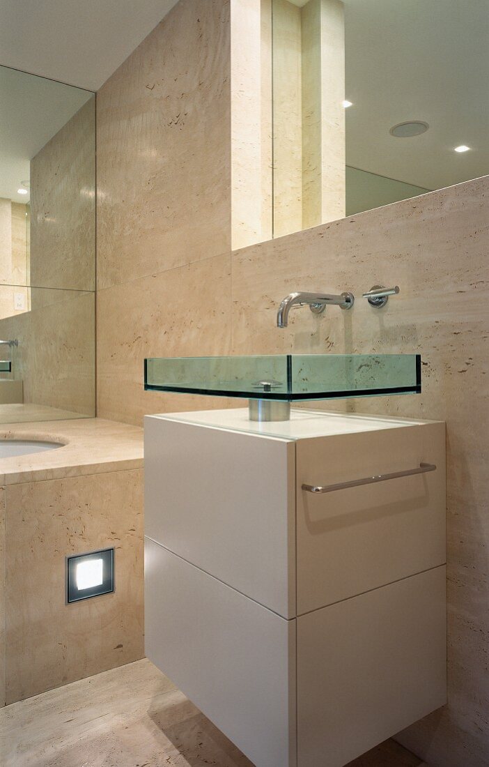 Extravagantes Waschbecken aus Glas auf weißem Unterschrank und Marmorverkleidung an Wand