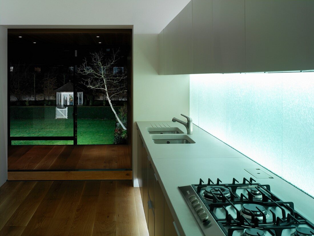 Moderne Küchenzeile mit hinterleuchteter Glaswand als Spritzschutz