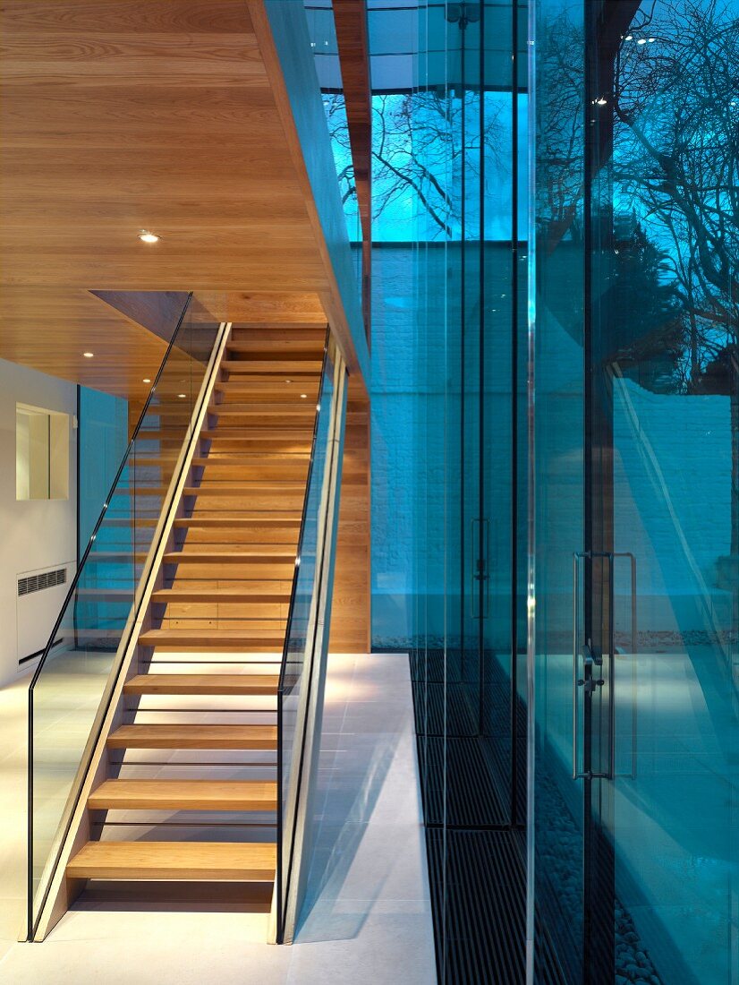 Foyer with staircase and glass balustrade beneath wood-clad ceiling