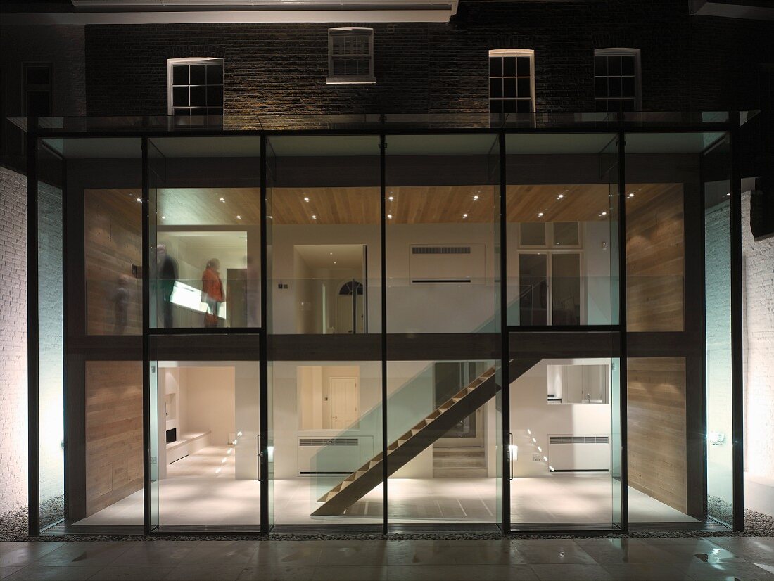Contemporary extension with glass wall and view of illuminated, two-storey stairwell