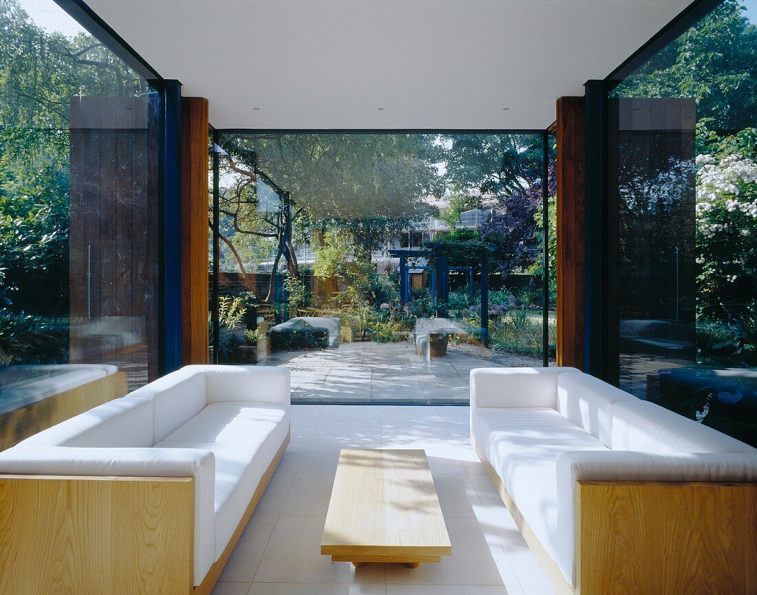 weiße Polstersofagarnitur im modernen verglasten Wohnraum und Gartenblick