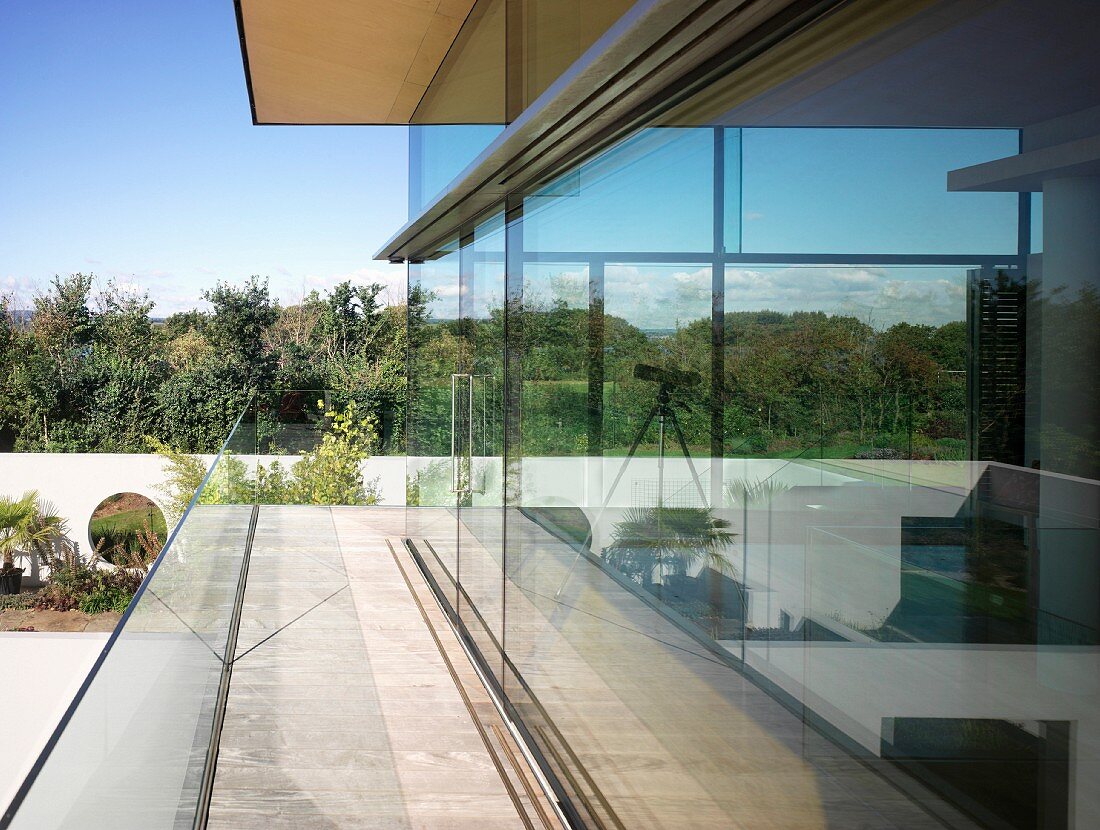 Umlaufende Terrasse vor Glasfassade eines zeitgenössischen Wohnhauses und Blick in Garten