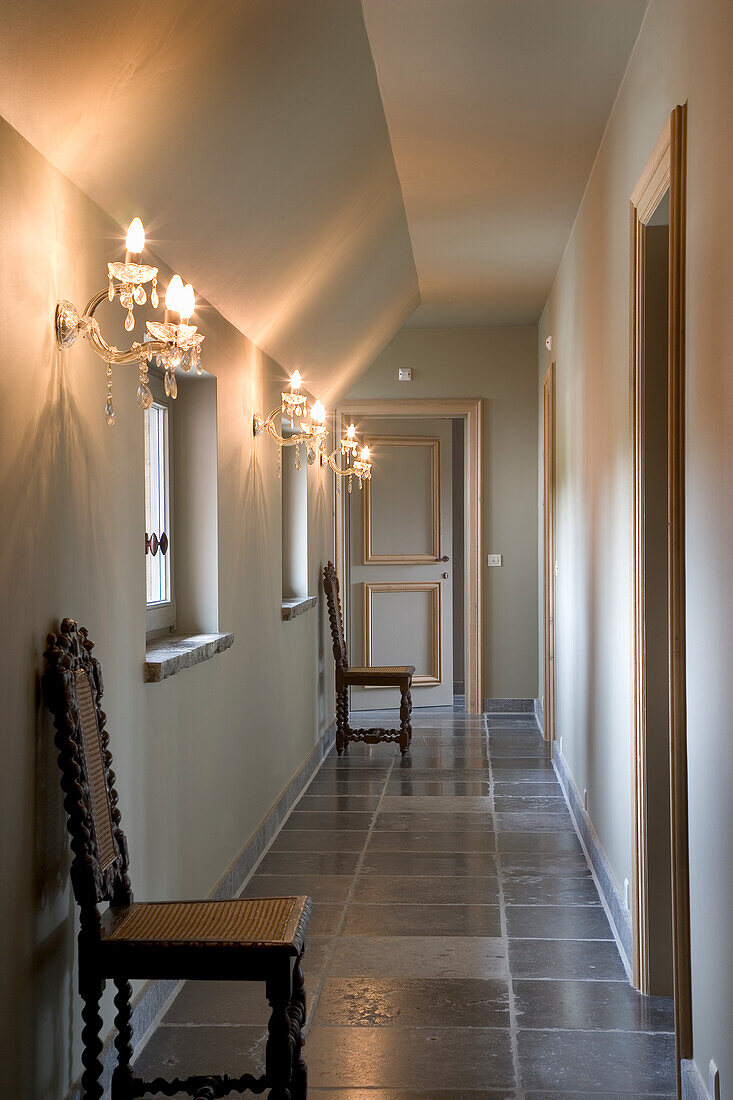 Hallway with chandeliers, baroque chairs and dark grey stone tiles