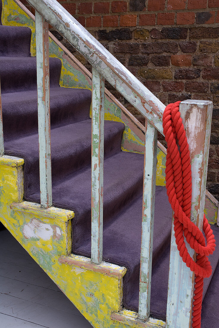 Abgeschabte Farbe an alter Holztreppe mit violettem Velourteppich auf den Stufen