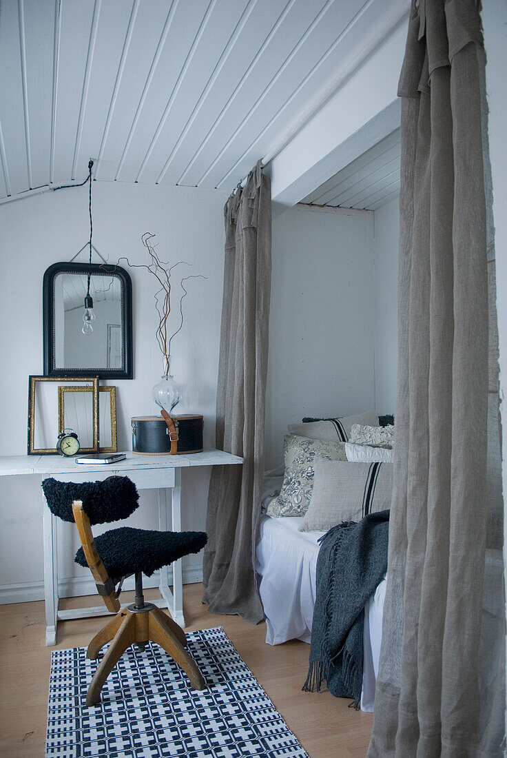 Schlafzimmer mit Tisch, Stuhl, Bett mit Zierkissen, weißen Wänden, weißer Holzdecke und Vintage-Deko